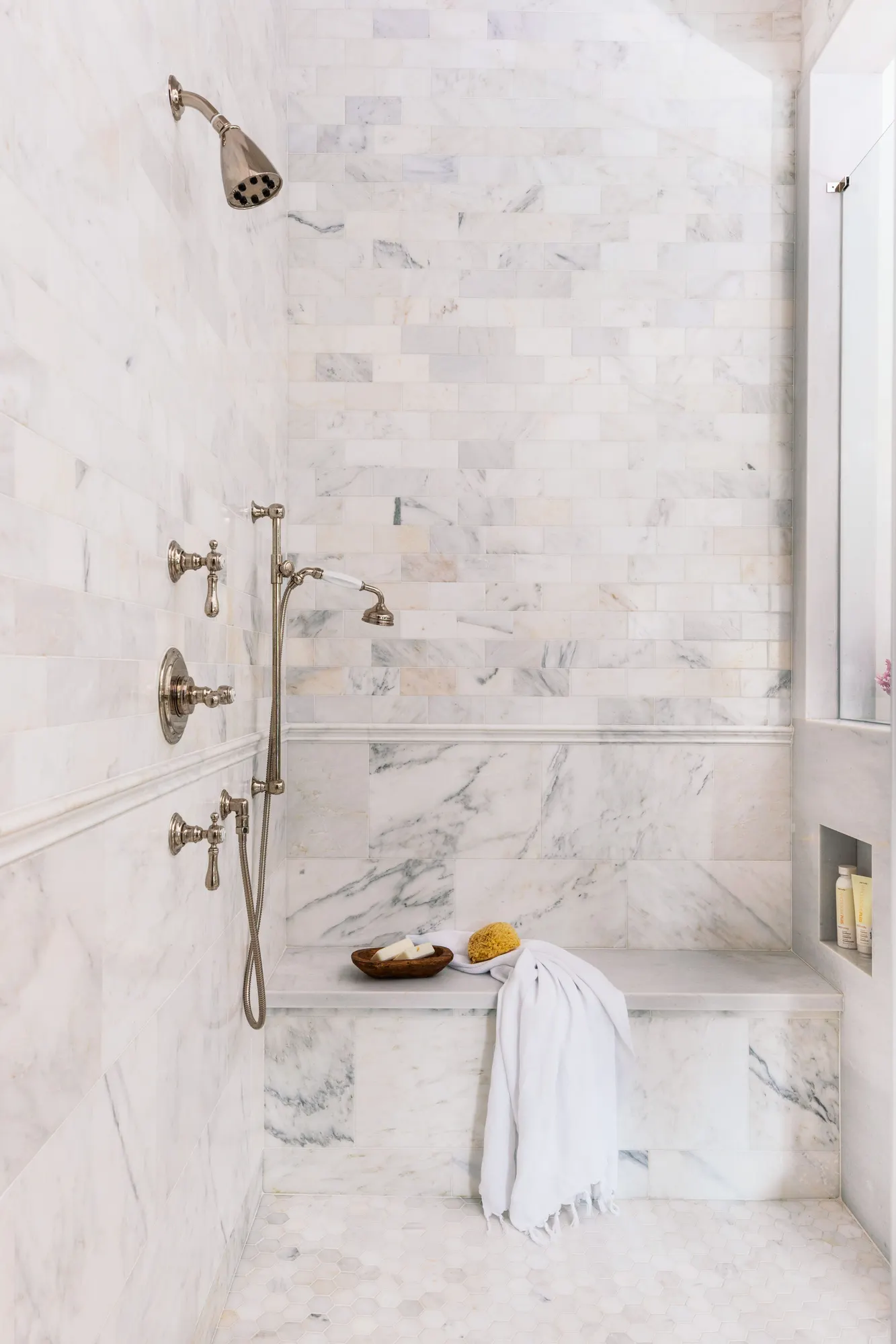 Marble walk-in shower with built-in bench and handheld shower on a slide bar
